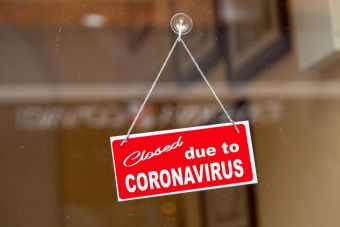 Red sign hanging at the glass door of a shop saying "Closed due to coronavirus". GETTY