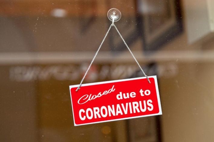 Red sign hanging at the glass door of a shop saying "Closed due to coronavirus". GETTY